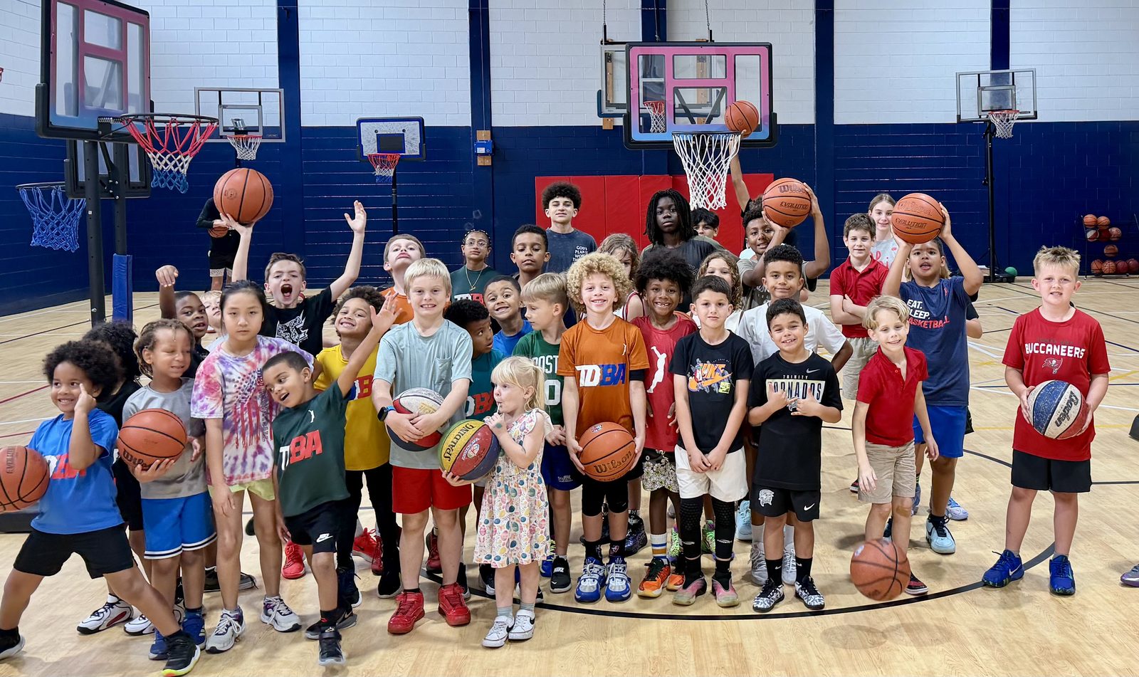 A gym full of TDBA campers holding basketballs up and celebrating