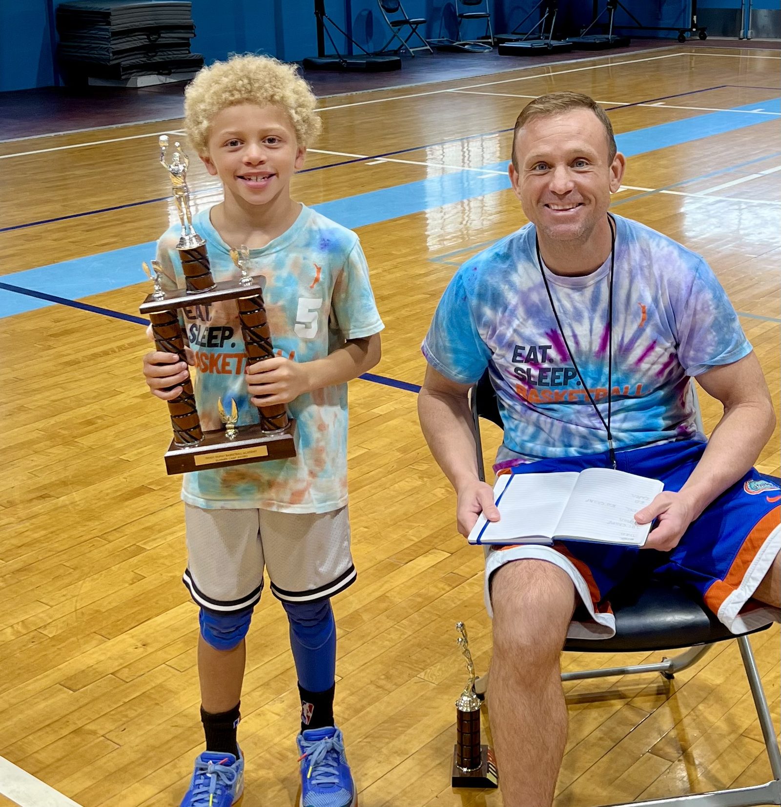 A TDBA camper holding the Summer Camp Award trophy next to Coach Teddy